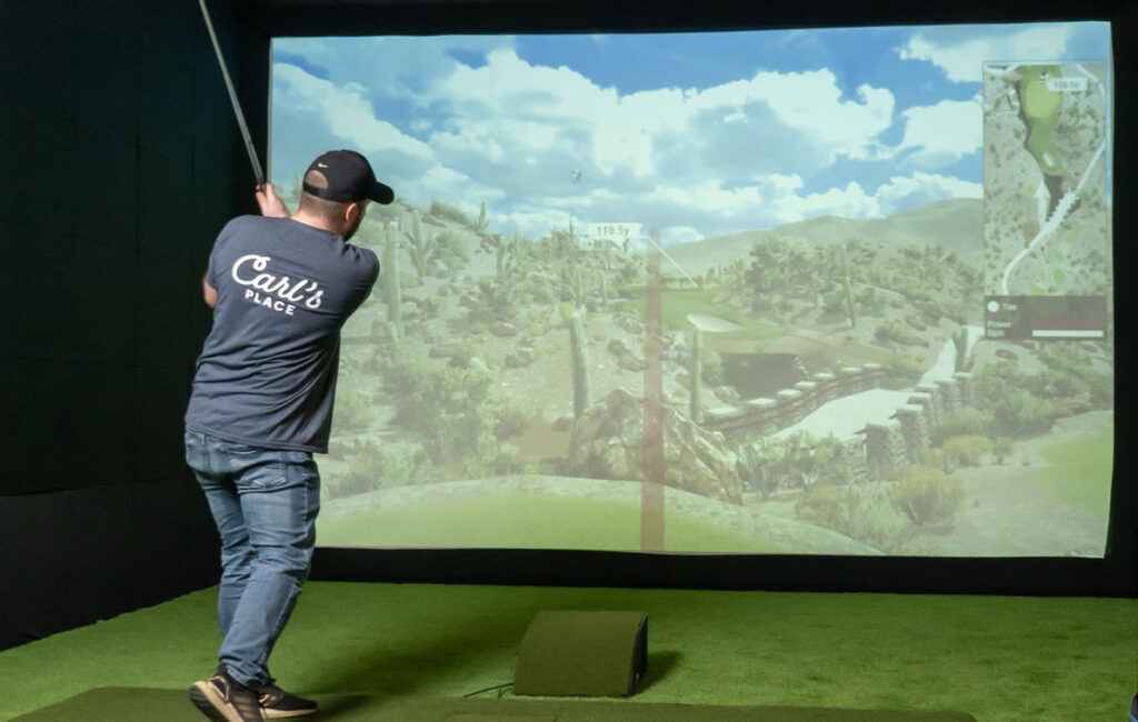 A backview of person hitting a shot in front of a projector in a golf simulator