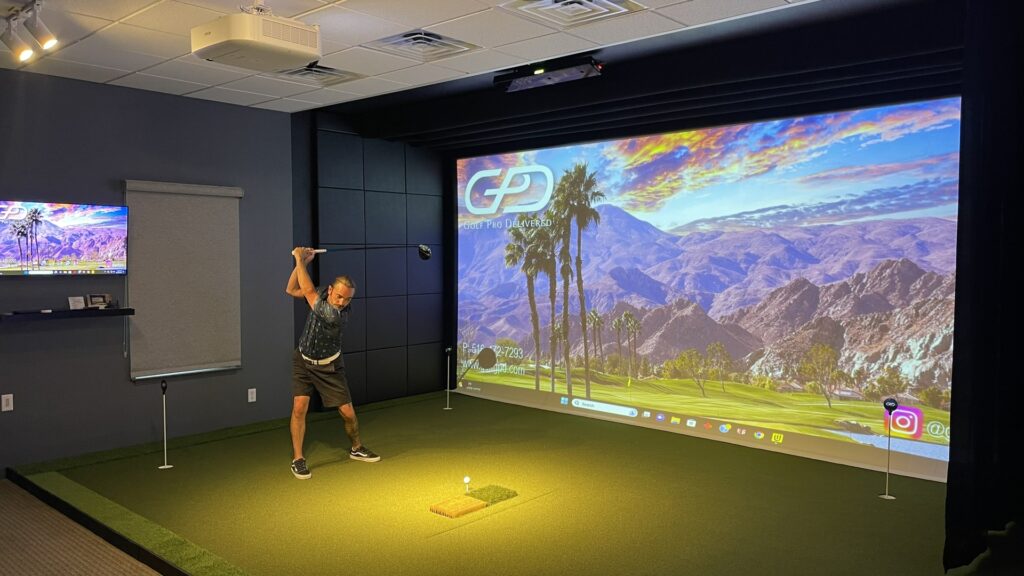 A person hitting a golf ball with a club inside a golf simulator projector