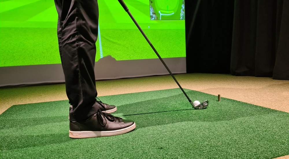 A lower angle view of a person hitting a shot in front of a golf simulator