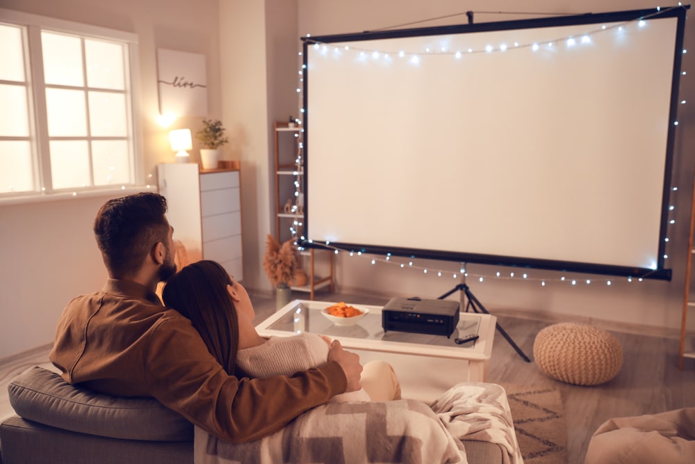 A view of a couple looking at a DIY projector at home with lights around