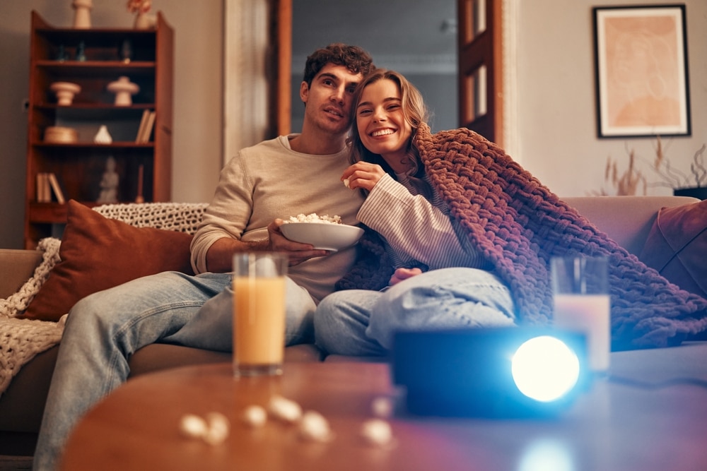 A view of a couple sitting together watching movie with the projector light on