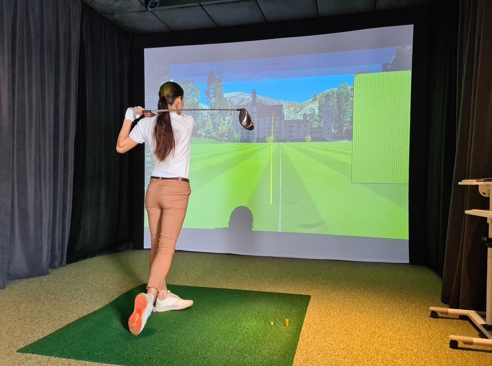 A view of a girl playing golf in front of a golf simulator