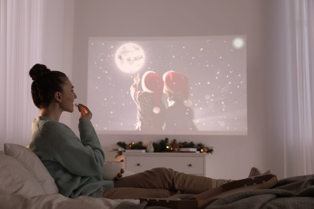 A view of a lady sitting in her bedroom watching movies on a projector