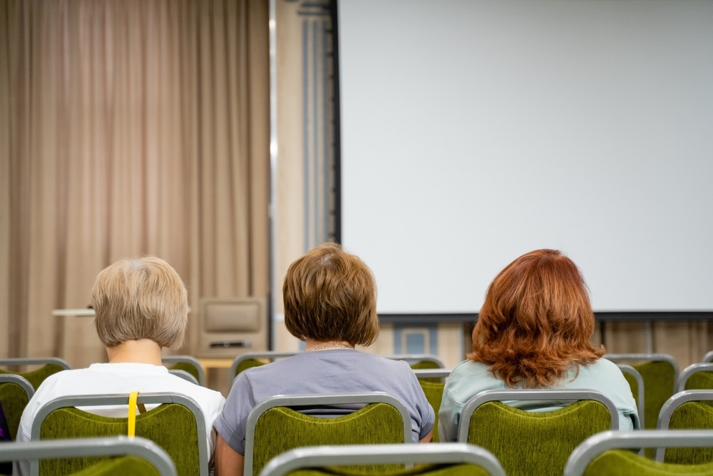 In A Conference Room Setting Three Audience Members Are Attentively