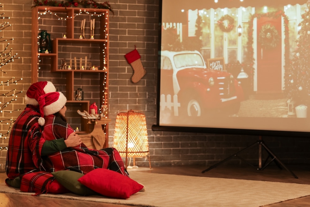 A view of a couple sitting wearing christmas hats and watching movie on a projector screen