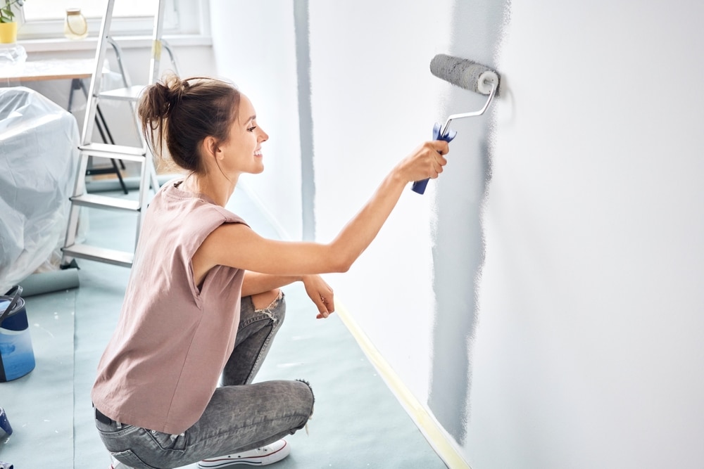 A side view of a woman painting a wall