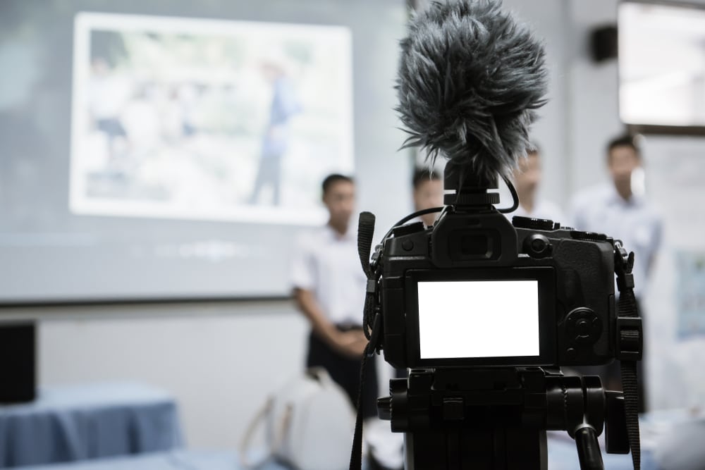 A view of a camera with a mic recording a projector screen