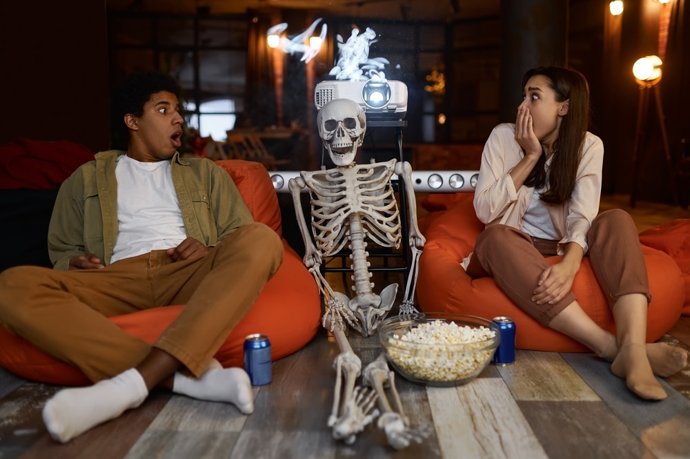 A view of a couple sitting with a spooky skeleton with a projector at back