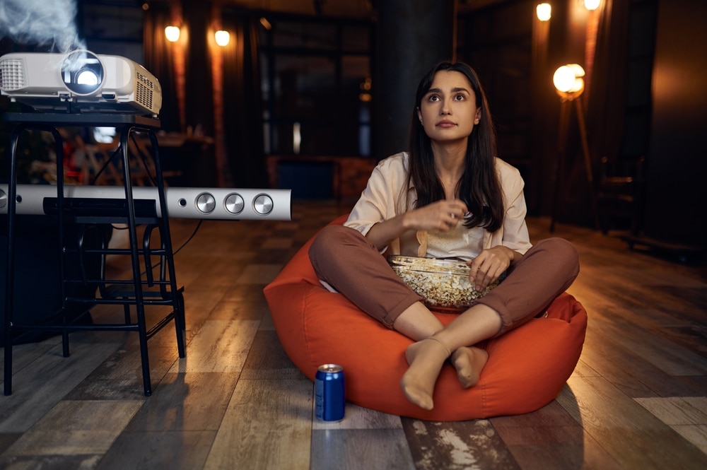 A view of a woman staring at front with popcorns and a projector on the side