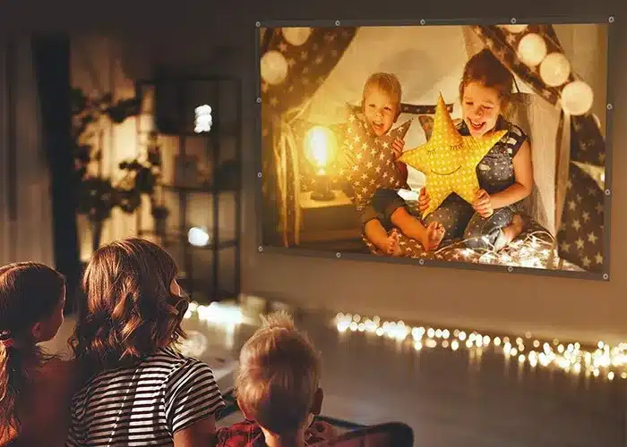 A family enjoying a cozy movie night watching a projector screen displaying children playing with glowing stars in a tent
