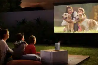 A family watching a movie outdoors with a projector featuring a woman and child with golden retrievers on the screen