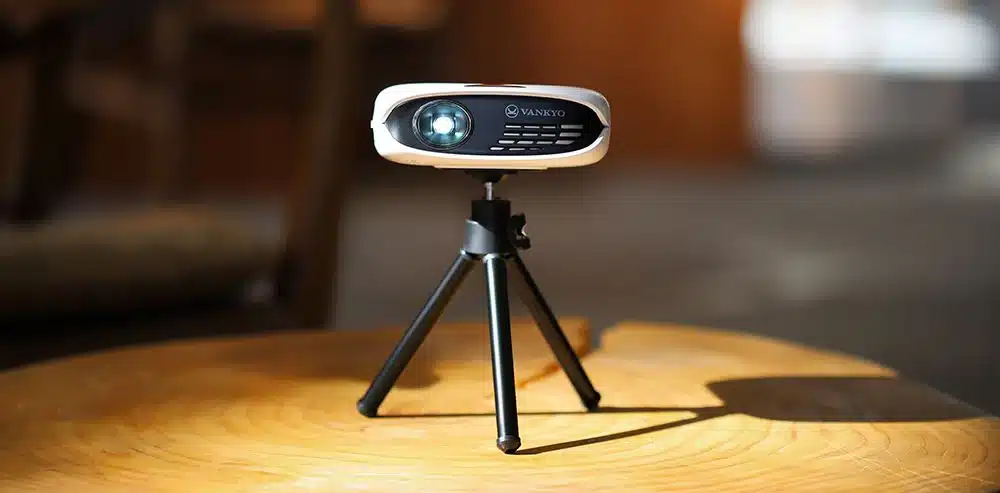 A portable VANKYO projector on a tripod placed on a wooden surface