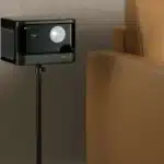 A projector placed on a sleek black floor stand next to a tan leather armchair projecting an image