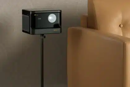 A projector placed on a sleek black floor stand next to a tan leather armchair projecting an image