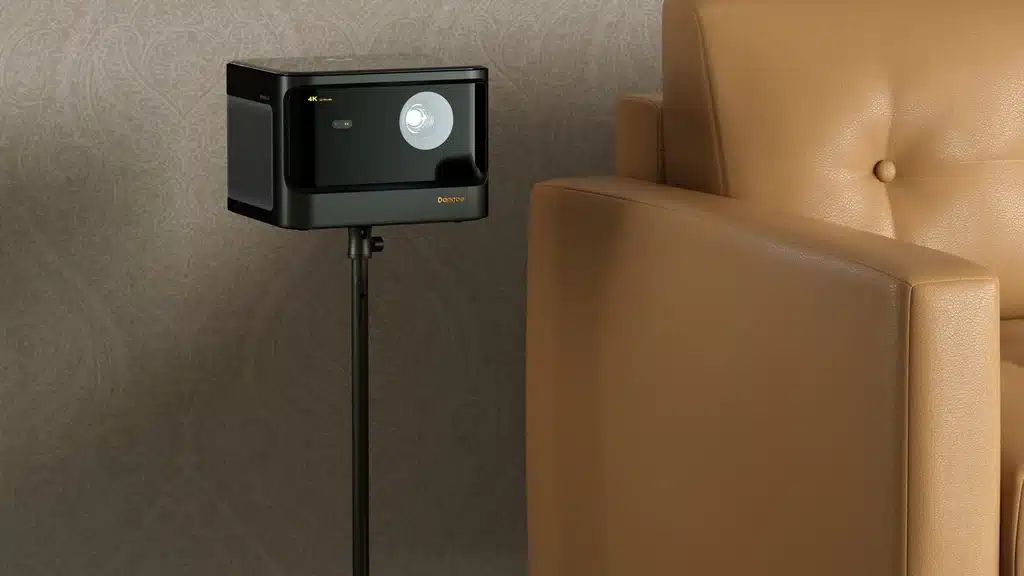 A projector placed on a sleek black floor stand next to a tan leather armchair projecting an image