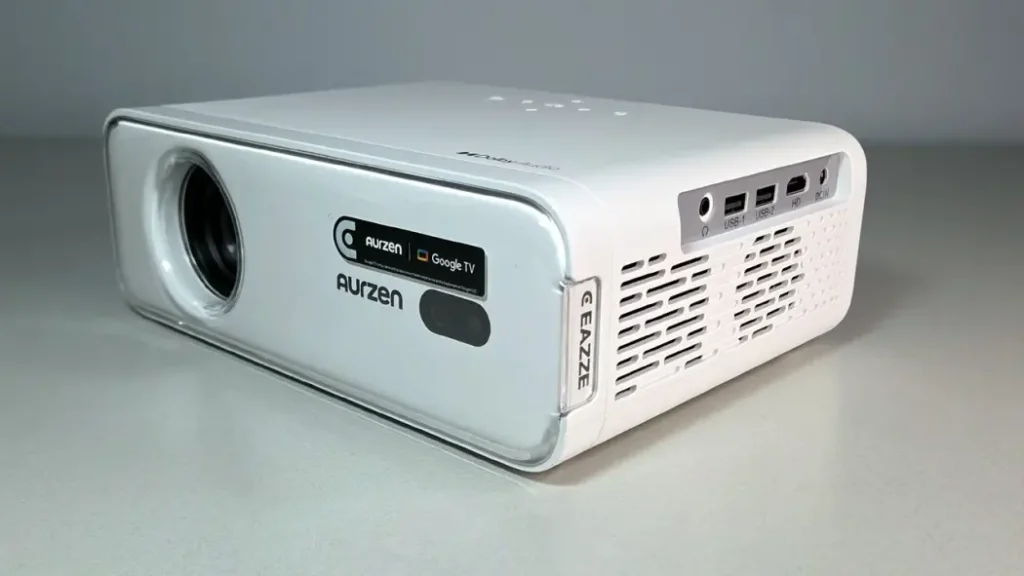 A white portable projector showing its lens and side ports with Aurzen and Google TV logos