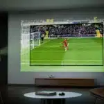 A projector displaying a soccer match on a wall in a living room setting