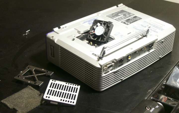 A projector with its back panel removed showing the fan and internal components